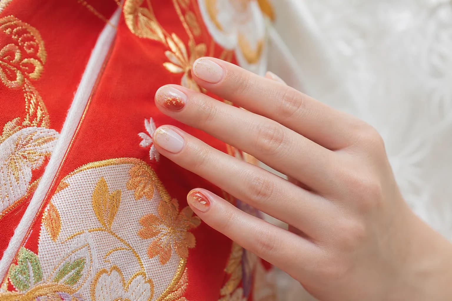 赤と金の刺繍が入った色打掛に添えた手元。朱赤と金箔を爪先から入れた、短めのラウンド型の和装ブライダルネイル
