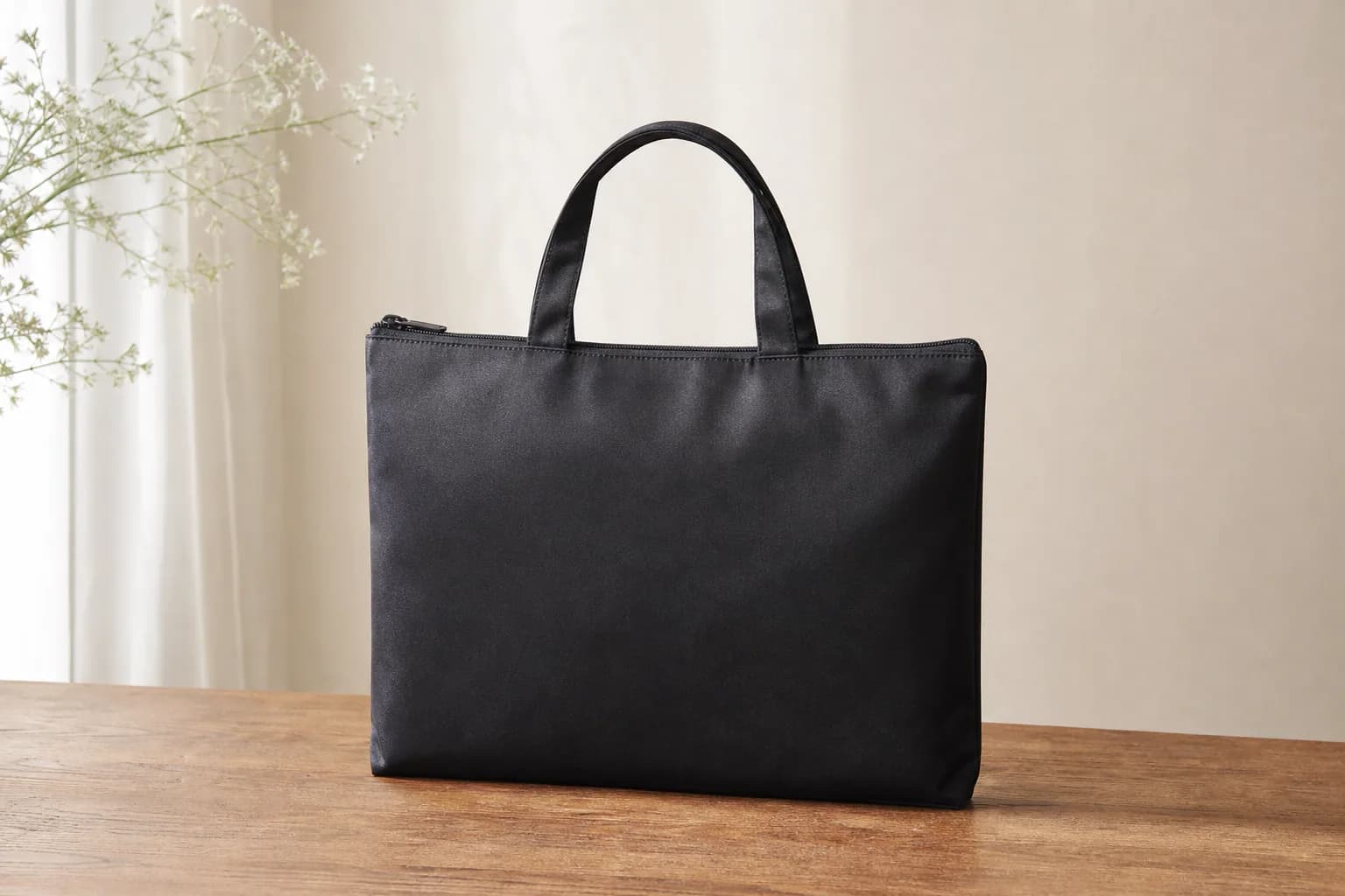 木製テーブルに置かれた黒い布製のサブバッグ。持ち手が2本ついた横長の形で、上部にファスナーがあり、荷物を入れなくても自立している